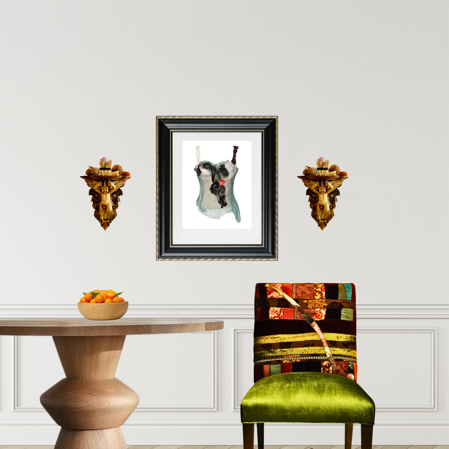 A framed art print featuring a black and white dog with a red bandana, displayed on a white wall in a styled room setting with a wooden table, a green velvet chair, and two bronze lion wall sculptures.